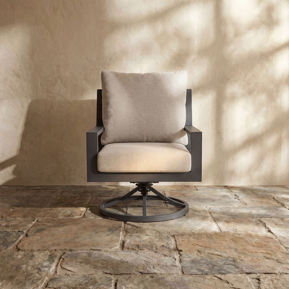 Sleek charcoal frame swivel patio chair with comfortable tan upholstery against a textured wall.