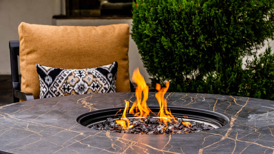 Dekton Laurent Top Firepit ignited next to a comfy patio chair and pillow