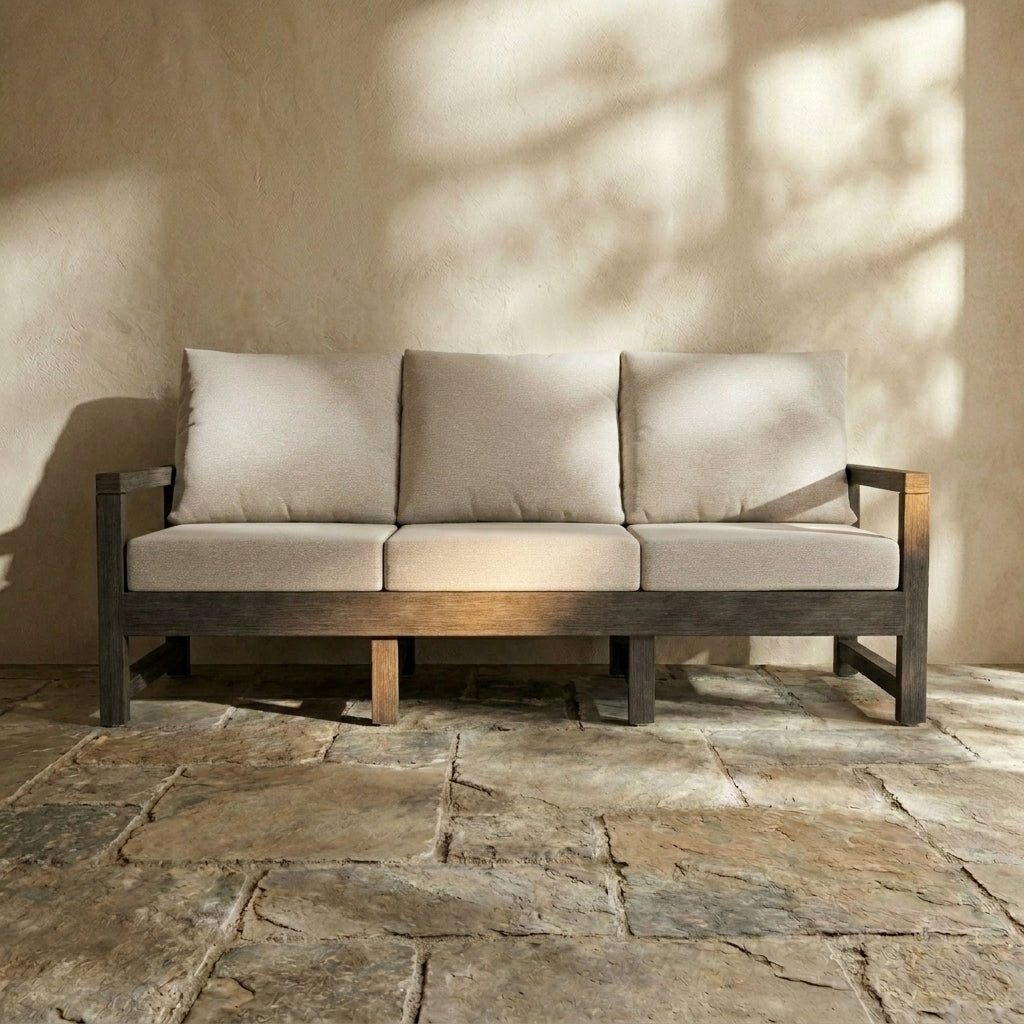 Paddy O' Furniture dark timber outdoor couch with neutral upholstered cushions in a bright courtyard setting.