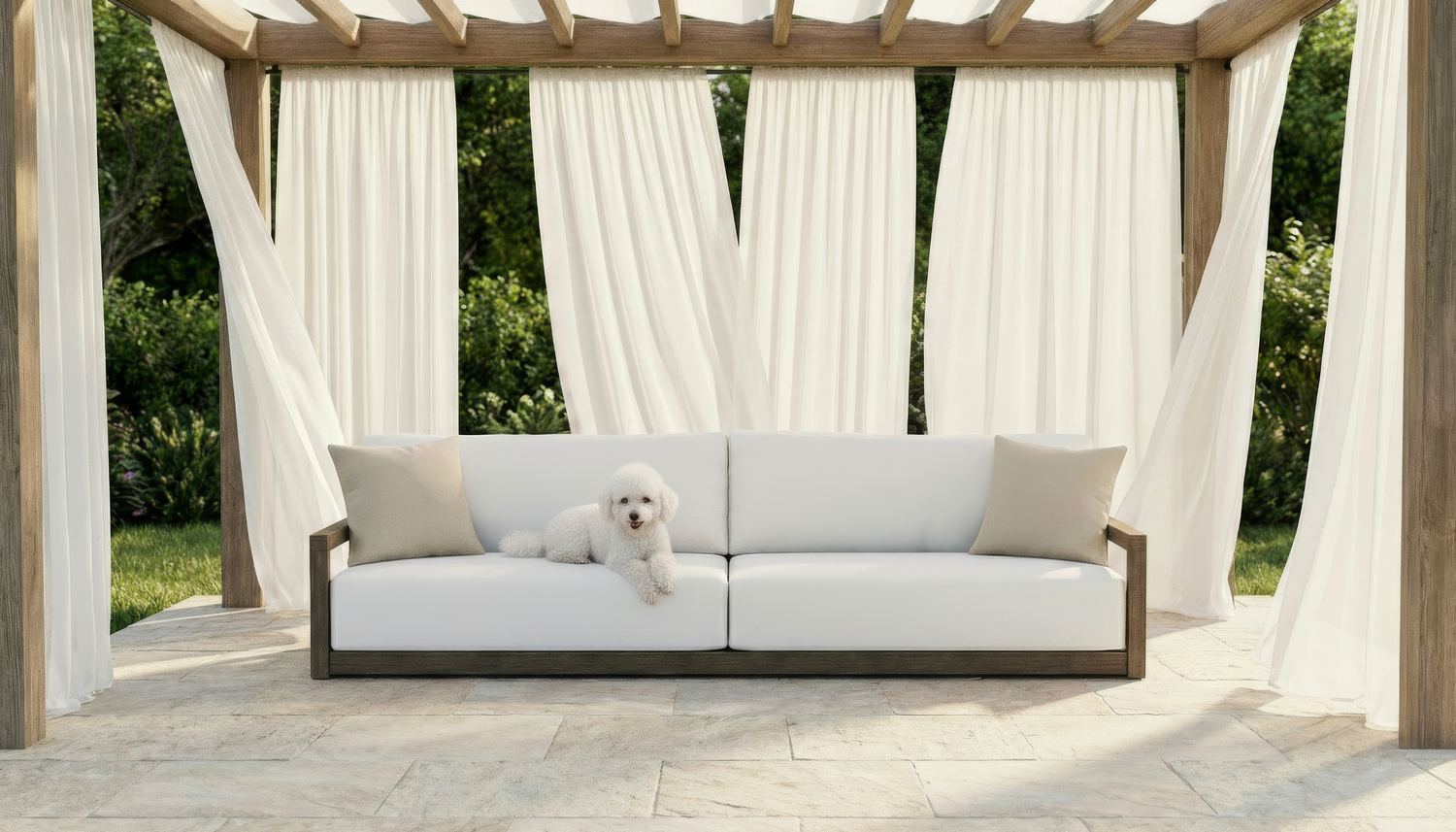 White outdoor sofa with beige cushions under a wooden pergola with white curtains.
