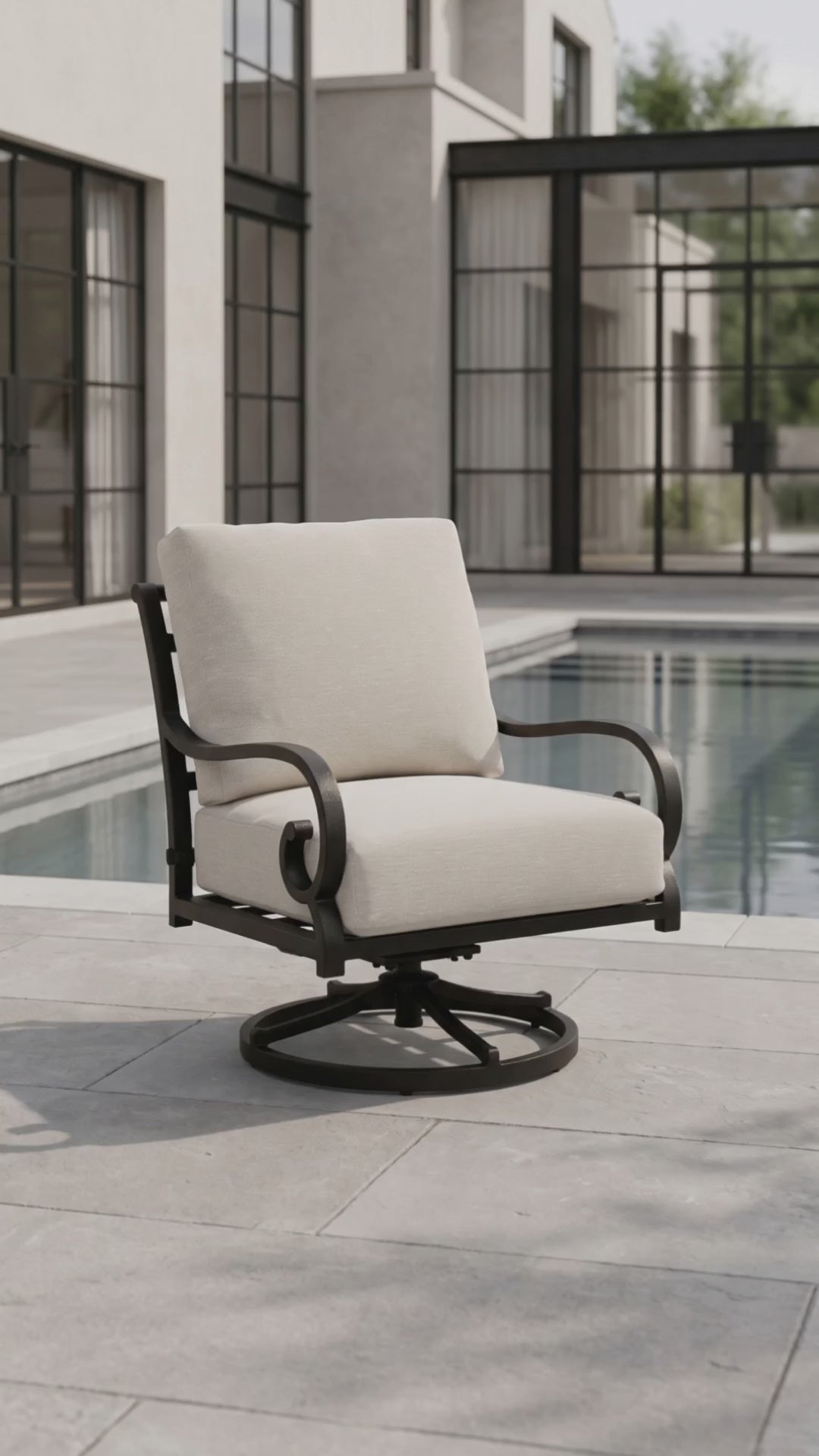 Outdoor swivel rocker patio chair with a black metal frame and cream cushions beside a modern swimming pool.