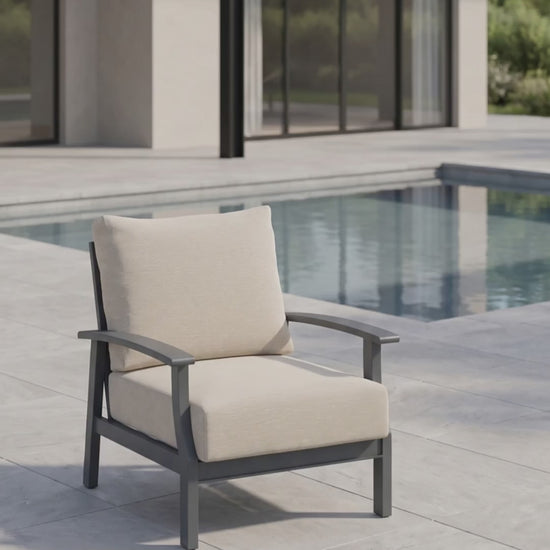 Rockport Club Chair with a black aluminum frame and cream cushions, shown poolside on a modern patio.