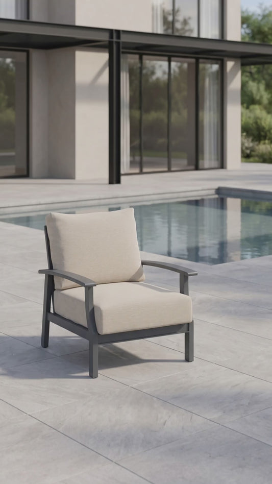 Rockport Club Chair with a black aluminum frame and cream cushions, shown poolside on a modern patio.