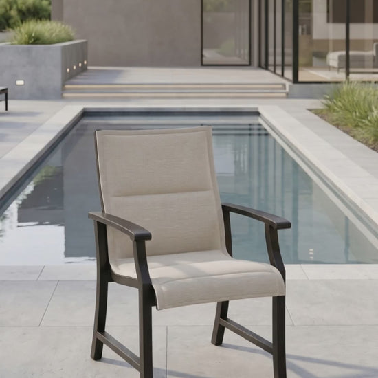 Outdoor dining chair with a padded oatmeal sling seat and back, ombre aluminum frame, shown on a modern poolside patio.