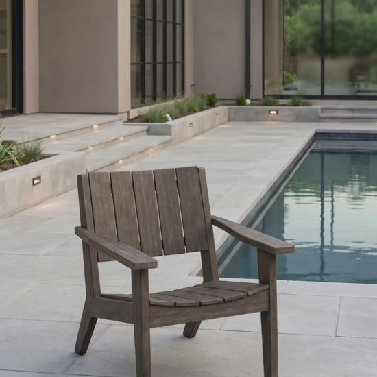 Weathered wood outdoor lounge chair displayed on a poolside patio in a modern backyard.