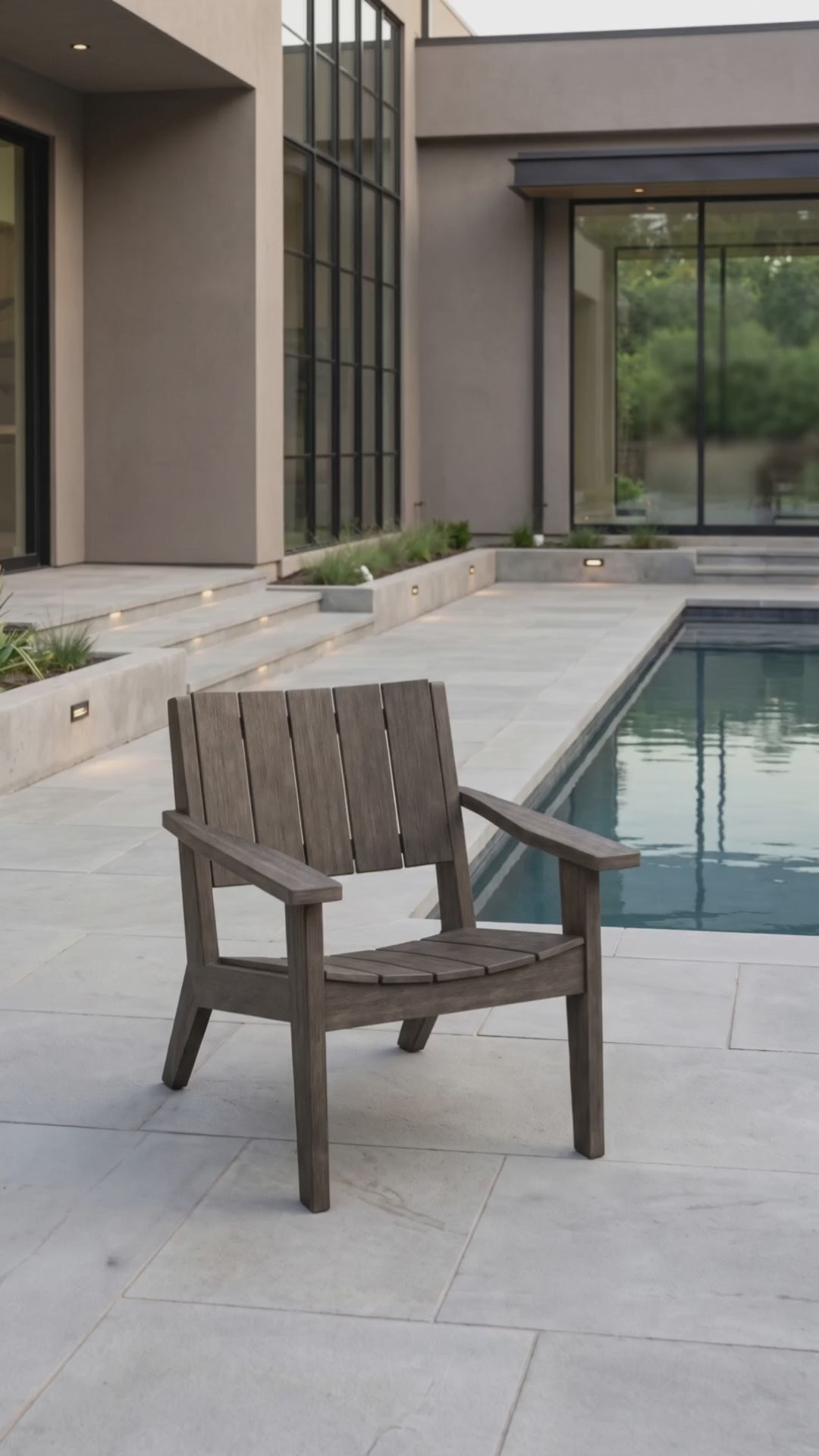 Weathered wood outdoor lounge chair displayed on a poolside patio in a modern backyard.