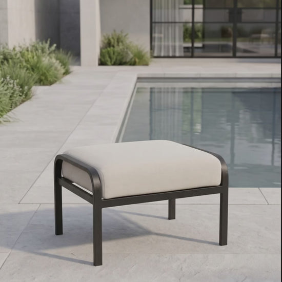 Modern outdoor ottoman with a cream cushion and black metal frame on a poolside patio.