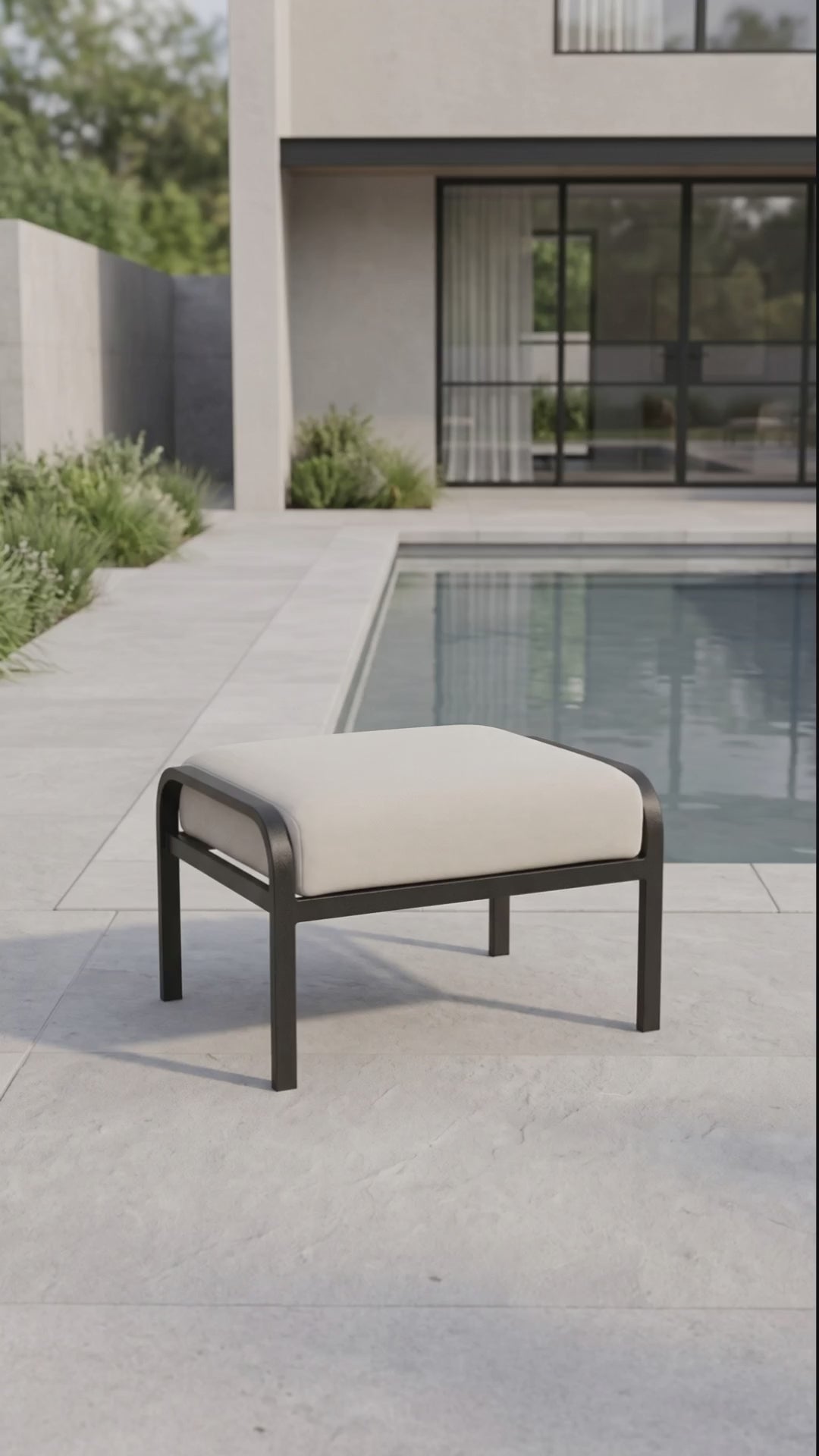 Modern outdoor ottoman with a cream cushion and black metal frame on a poolside patio.